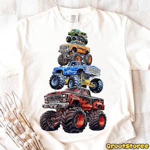 May include: White t-shirt featuring a graphic of five colorful monster trucks stacked on top of each other. The trucks are in shades of red, blue, orange, and green, with large tires. The text "GrootStoree" is at the bottom right.