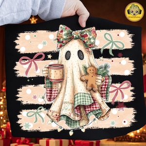 May include: A black t-shirt featuring a graphic of a ghost wearing a floral bow, holding a mug and a gingerbread cookie. The ghost is draped in a patchwork blanket with red, green, and cream colors, surrounded by string lights and bows.