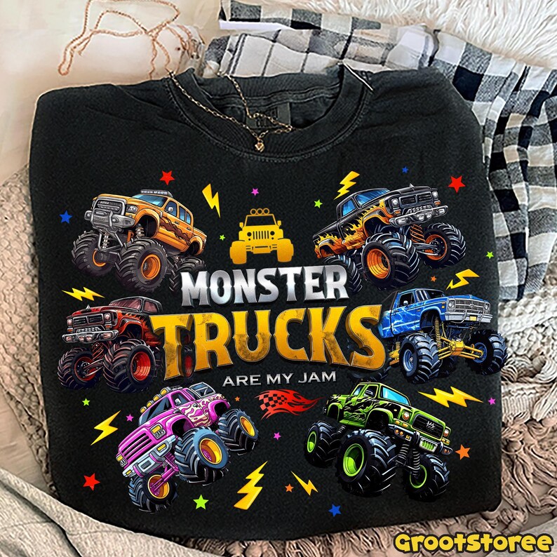 May include: Black sweatshirt with a colorful graphic of monster trucks. The design includes the text "MONSTER TRUCKS ARE MY JAM" with various monster truck illustrations in orange, red, blue, green, and pink. The design also includes lightning bolts and stars.