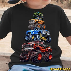 May include: Black t-shirt featuring a stack of colorful monster trucks. The trucks are red, orange, blue, and green, with large tires and detailed graphics. The text "GrootStoree" is at the bottom right.
