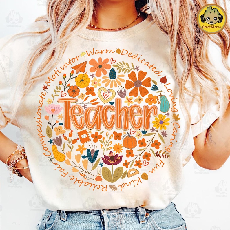 May include: Cream-colored t-shirt with a floral design surrounding the word "Teacher" in orange. The design includes flowers, leaves, and the words "Motivator", "Warm", "Dedicated", "Loving", "Caring", "Fun", "Kind", "Reliable", "Fair", and "Compassionate".