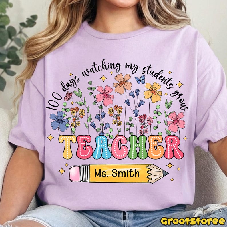 May include: A light purple t-shirt with the text "100 days watching my students grow" above a colorful floral design and the word "TEACHER" in large, bubble letters. A yellow pencil with the name "Ms. Smith" is below the word "TEACHER".