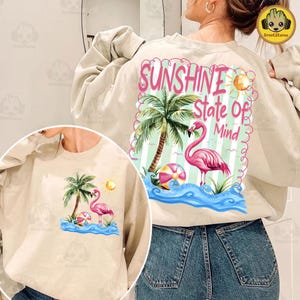 May include: Beige sweatshirt with a tropical design featuring a pink flamingo, palm tree, beach ball, and the text "Sunshine State of Mind." The design is framed with a scalloped border and a sun graphic.