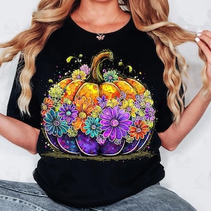 May include: Black t-shirt featuring a vibrant, colorful pumpkin design. The pumpkin is adorned with an array of flowers in shades of purple, orange, yellow, and blue. The design has a whimsical, artistic style, perfect for fall.