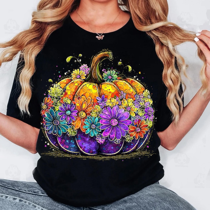May include: Black t-shirt featuring a vibrant, colorful pumpkin design. The pumpkin is adorned with an array of flowers in shades of purple, orange, yellow, and blue. The design has a whimsical, artistic style, perfect for fall.
