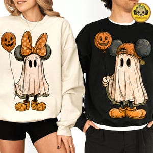 Könnte beinhalten: Ein cremefarbenes Sweatshirt mit einem Geist, der eine gepunktete Schleife und orangefarbene Schuhe trägt und einen Kürbisballon hält, sowie ein schwarzes Sweatshirt mit einem Geist, der eine Baseballkappe und orangefarbene Schuhe trägt.