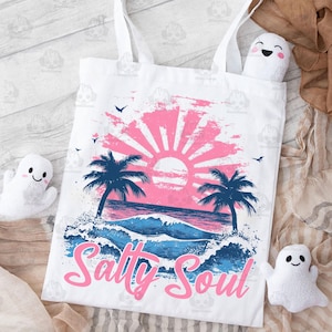 May include: White tote bag with a pink and blue sunset graphic, palm trees, and ocean waves. The text "Salty Soul" is written in pink letters.