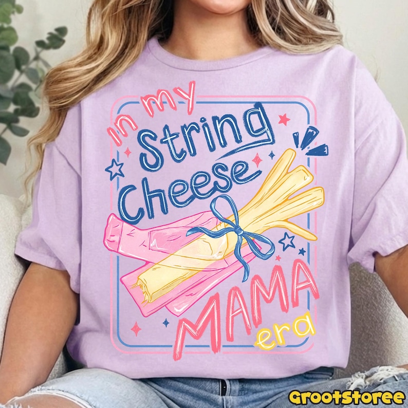 May include: A light purple t-shirt with a graphic design featuring string cheese and the text "In my String Cheese Mama Era". The design includes a bundle of string cheese tied with a blue ribbon.