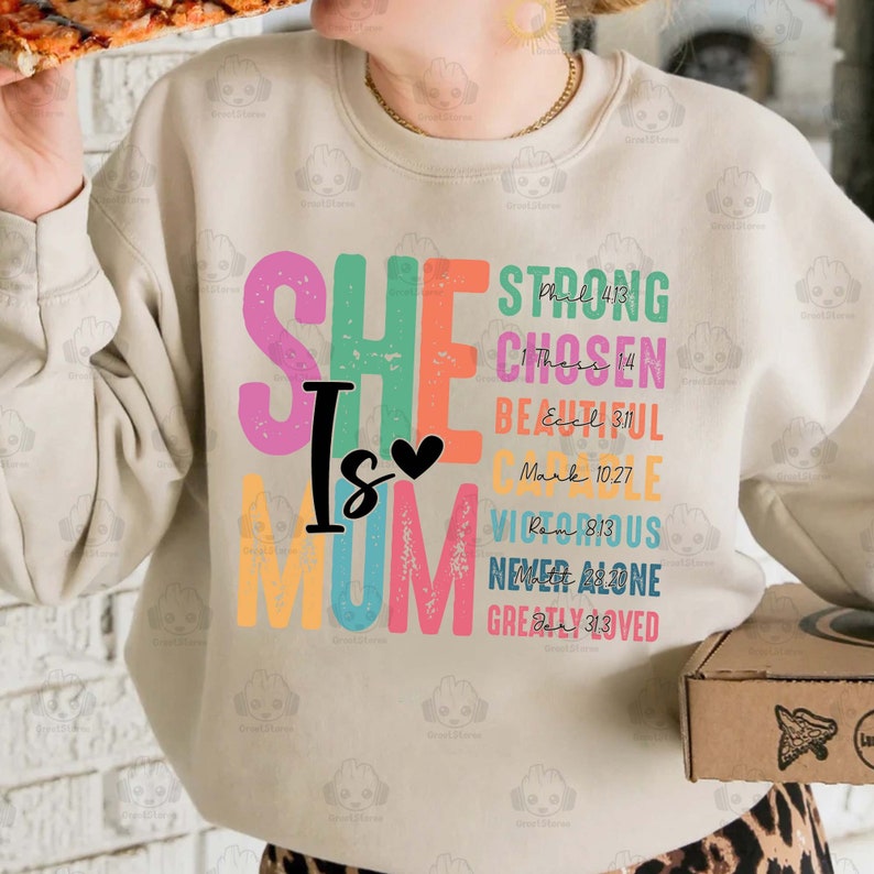 K&ouml;nnte beinhalten: Ein beiger Pullover mit den Worten "SHE IS MOM" in bunten Buchstaben. Die Buchstaben sind mit einem abgenutzten, Vintage-Look verziert. Jeder Buchstabe ist mit einem Bibelvers gepaart.