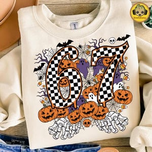 May include: Cream-colored sweatshirt with a Halloween-themed design. The design features the numbers "67" in a black and white checkered pattern, surrounded by jack-o'-lanterns, ghosts, bats, spiderwebs, and candy corn.