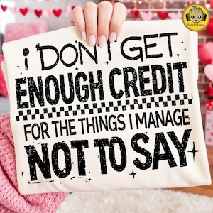 May include: Cream-colored t-shirt with the text "I DON'T GET ENOUGH CREDIT FOR THE THINGS I MANAGE NOT TO SAY" in black. The shirt is held up by a person.