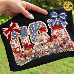 Puede incluir: Un textil negro con la palabra "USA" aplicada en tela roja, blanca y azul. Las letras están decoradas con motivos florales, estrellas y lazos, y están adornadas con un borde floral. Las letras también están decoradas con una variedad de flores.