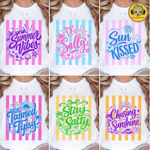 Op de afbeelding: Witte T-shirts met zomerse afbeeldingen. Ontwerpen zijn onder meer "Summer Vibes", "Sally", "Sun Kissed", "Tanned Tipsy", "Stay Salty" en "Chasing Sunshine". Elk shirt heeft verticale strepen in verschillende kleuren en decoratieve elementen zoals bloemen en schelpen.