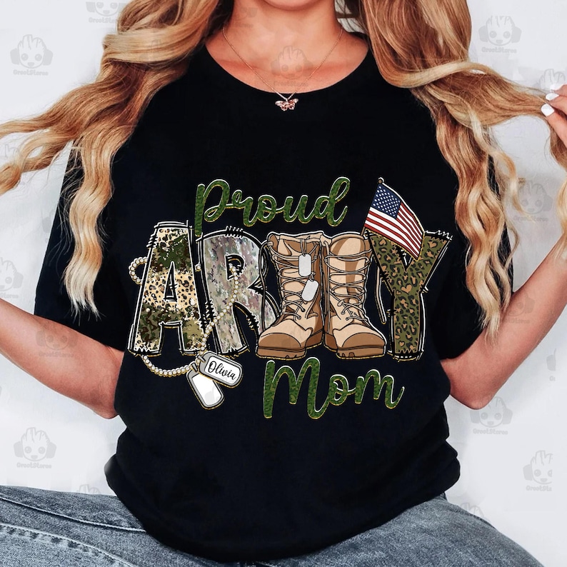 May include: Black t-shirt with a green, white, and red camouflage design. The text "Proud Army Mom" is written in green letters. A small American flag is in the upper right corner. The text "Olivia" is written on a dog tag.