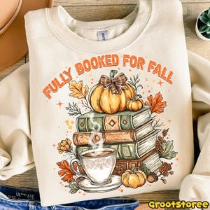 May include: Cream sweatshirt with the text "FULLY BOOKED FOR FALL" in orange. The graphic features a stack of books, pumpkins, autumn leaves, and a cup of coffee. A cozy design for autumn and book lovers.
