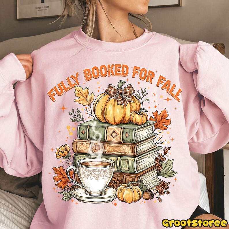 May include: Pale pink sweatshirt with the words "FULLY BOOKED FOR FALL" in orange. The design includes a pumpkin, books, a cup of coffee, and autumn leaves. A cosy design for the autumn season.