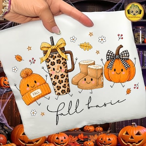 Puede incluir: Una camiseta blanca con un estampado gráfico de un gorro de punto naranja sonriente con la palabra FALL, un vaso con estampado de leopardo y un lazo amarillo, botas de invierno beige y una calabaza naranja sonriente con un lazo a cuadros, con el texto fall basic.