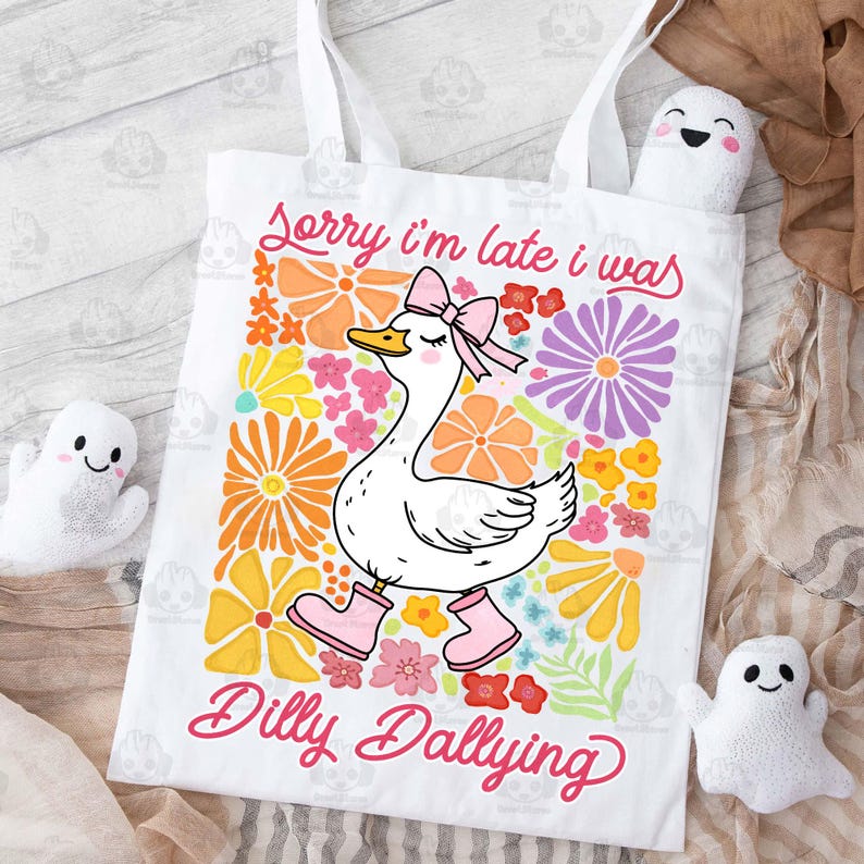 Op de afbeelding: Witte tote bag met een roze en witte gans illustratie en de tekst "Sorry, ik ben te laat, ik was aan het dralen". De gans draagt roze schoenen en is omringd door kleurrijke bloemen.
