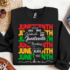 May include: Black sweatshirt with a colorful Juneteenth design. The design includes the words "Juneteenth" in red, green, and yellow, along with the phrases "Freeish Since 1865" and "Celebrate Freedom Day". A silhouette of a person is also included.