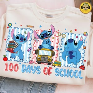 May include: A cream-coloured sweatshirt with a colourful graphic of the character Stitch from Lilo & Stitch. The design includes Stitch with books, on a school bus, and waving, with the text "100 Days of School".