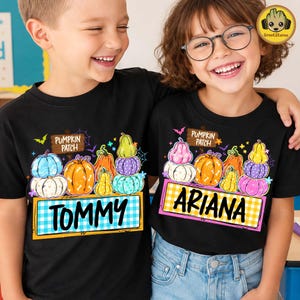 Puede incluir: Dos camisetas negras con un gráfico colorido de calabazas apiladas, un letrero de madera que dice PUMPKIN PATCH y una pancarta rectangular a cuadros con los nombres TOMMY y ARIANA impresos en letras negras en cada camiseta.