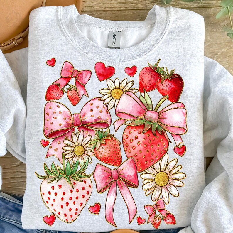 May include: A gray sweatshirt with a pink and red strawberry and bow design. The design includes hearts, flowers, and glitter accents.
