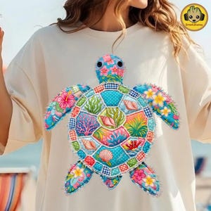 May include: Cream-colored t-shirt featuring a colorful, patchwork-style sea turtle design. The turtle's shell is a mosaic of patterns and colors, including floral prints, polka dots, and seashell motifs. The design is centered on the shirt.