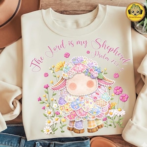 May include: Cream-colored sweatshirt featuring a colorful patchwork sheep design surrounded by flowers. The text "The Lord is my Shepherd Psalm 23:1-2" is written in pink script across the top. A whimsical and inspirational design.