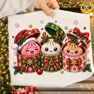 May include: A white fabric item featuring a graphic print of three smiling, glittery dumpling characters emerging from festive gift boxes. The boxes are decorated with red and green patterns, bows, holly, and snowflakes, with small gold stars scattered around.