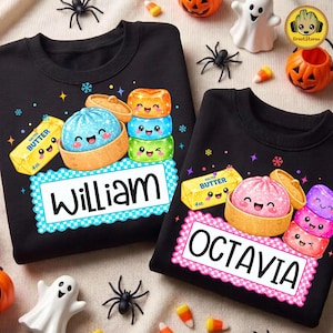 Könnte beinhalten: Zwei schwarze Sweatshirts mit Rundhalsausschnitt und grafischen Aufdrucken von Cartoon-Lebensmitteln mit Gesichtern. Ein Oberteil zeigt den Namen William, das andere Octavia. Jedes Design enthält ein Stück gesalzene Butter, einen Knödel und Bonbons.