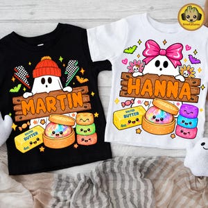 Puede incluir: Una camiseta negra con un fantasma con gorro naranja y una camiseta blanca con un fantasma con lazo rosa. Ambas muestran un letrero de madera con los nombres MARTIN y HANNA, además de ilustraciones de mantequilla, dim sum y dulces coloridos.