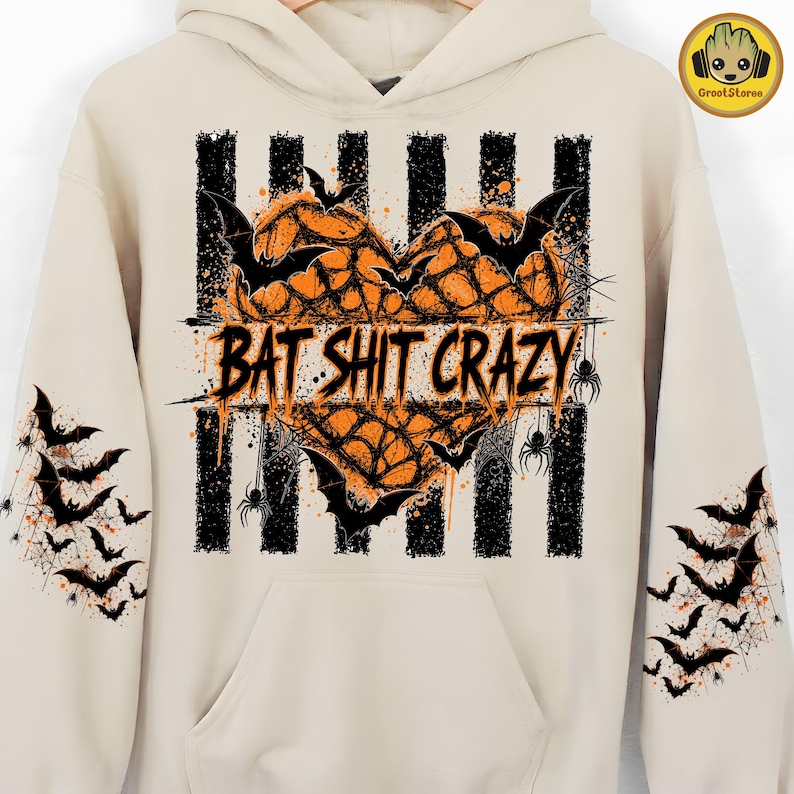 May include: A beige hooded sweatshirt featuring a central graphic of an orange heart filled with spiderwebs and black bats. The text BAT SHIT CRAZY is printed across the center over black vertical stripes. Both sleeves feature black bat silhouettes.