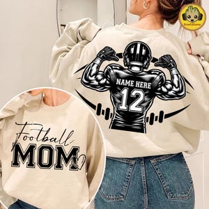May include: Beige sweatshirt with a black and white football player graphic on the back, featuring the text "NAME HERE" and the number "12". A smaller beige sweatshirt with the text "Football MOM" is visible in the lower left corner.