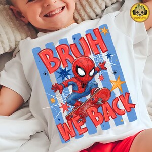 May include: A white t-shirt featuring a graphic of a cartoon Spider-Man character riding a red skateboard. The design includes blue vertical stripes, yellow stars, white spiderwebs, and the red text "BRUH WE BACK" in a bold, bubbly font.