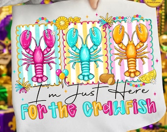 May include: White sweatshirt with a colorful graphic of three lobsters in pink, blue, and orange, each set against a different striped background. The text "I'm Just Here For The Crawfish" is written below the lobsters.