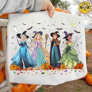 May include: A white tote bag featuring four cartoon princesses dressed as witches, with pumpkins, ghosts, bats, and spiderwebs. The princesses are in colorful gowns and witch hats, holding wands, a broom, and a book. The GrootStore logo is in the upper right corner.