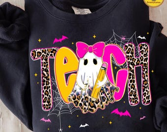 Może przedstawiać: Czarna bluza z motywem Halloween. Słowo "TEACH" jest wyświetlane z nadrukiem w cętki i różowymi literami. Postać ducha trzymająca ołówek znajduje się na środku. Nietoperze, pajęczyny i gwiazdy dopełniają projekt.