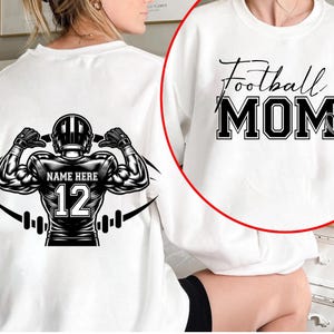 May include: White sweatshirt with a black and white graphic of a football player flexing, with the text "NAME HERE" and the number "12". The other side of the sweatshirt has the words "Football MOM" in black.