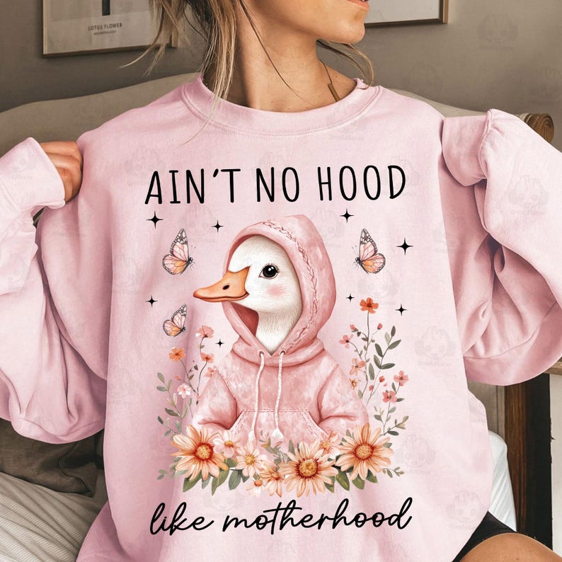 May include: Pink sweatshirt with a graphic of a duck wearing a pink hoodie and the text "Ain't no hood like motherhood" with flowers surrounding the duck.