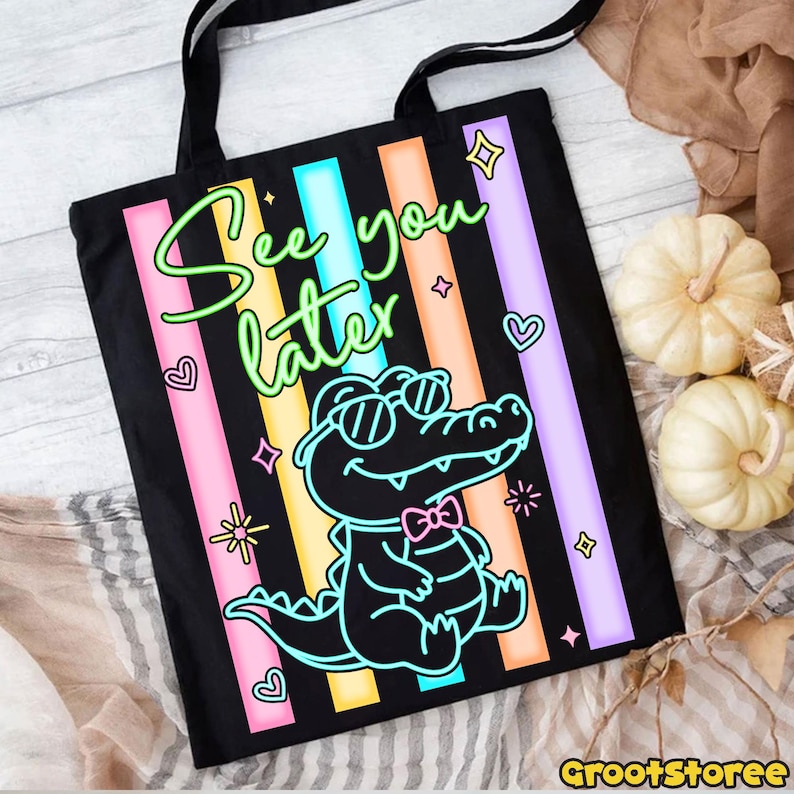 May include: Black tote bag with a colorful design featuring a cartoon alligator wearing sunglasses and a bow tie. The text "See you later" is written in a neon green font, with pink, blue, orange, and purple stripes.