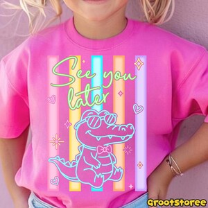 May include: Pink sweatshirt with a neon graphic of an alligator wearing sunglasses and a bow tie, with the text "See you later." The design includes colorful vertical stripes, hearts, and stars.