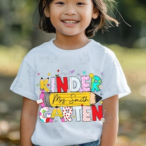 May include: A white t-shirt with a colourful graphic that says "Kindergarten" with a pencil and the text "Mrs. Smith" on it.