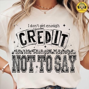 Pode incluir: Camiseta creme com a frase "I don't get enough CREDIT for the things I manage NOT TO SAY" em fonte preta desgastada. A camiseta tem gola redonda e mangas curtas. O design está centrado na frente.