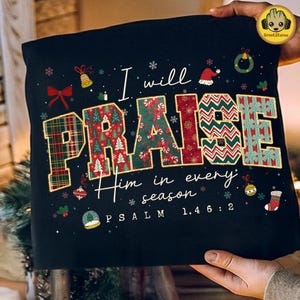 May include: Black cushion featuring the words "I will PRAISE Him in every season" in white, with festive Christmas designs. The word "PRAISE" is in a plaid, Christmas tree, and gift pattern. Psalm 146:2 is at the bottom.