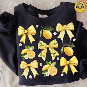 May include: Black sweatshirt with a yellow lemon and bow pattern. The lemons are illustrated with green leaves and the bows are yellow and white gingham.