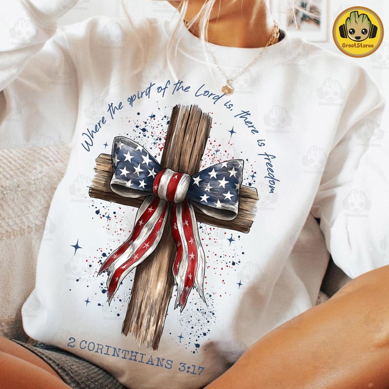 Może przedstawiać: Biała bluza z drewnianym krzyżem ozdobionym kokardą w barwach amerykańskiej flagi. Tekst brzmi: "Where the spirit of the Lord is, there is freedom" i "2 Corinthians 3:17".