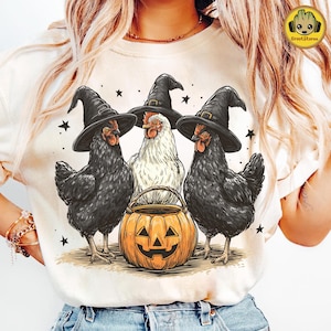 May include: A cream-colored t-shirt featuring a Halloween design. Three chickens wearing black witch hats stand around a carved pumpkin. The chickens are black and white, with stars scattered around the design. The GrootStore logo is in the upper right corner.