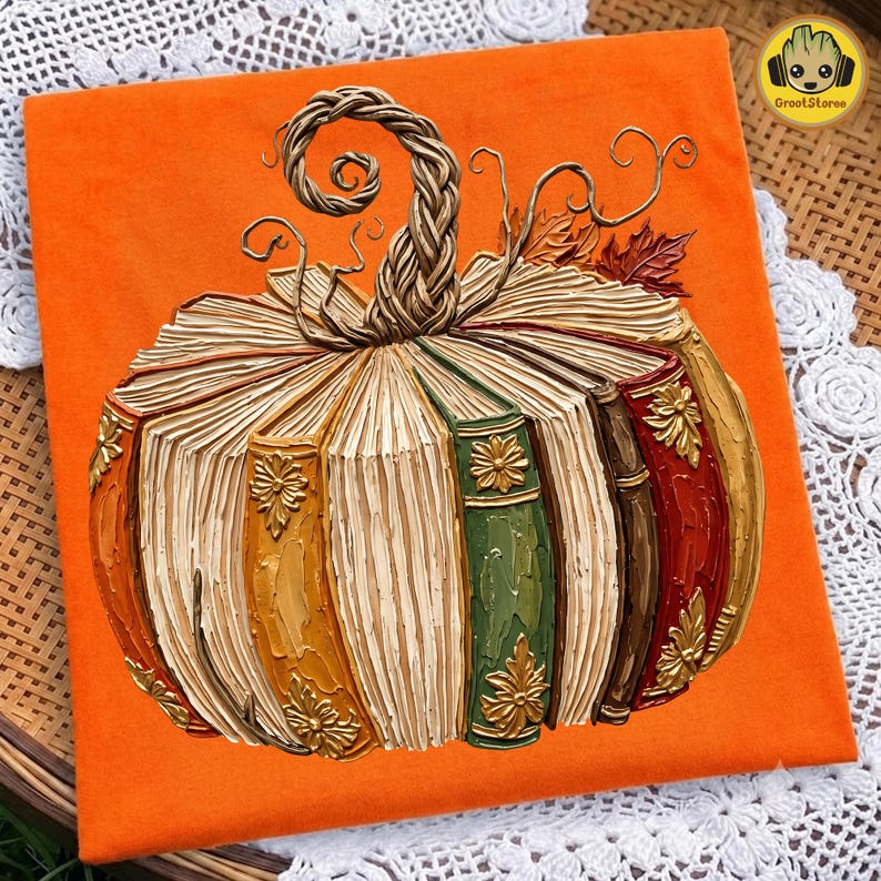 Peut inclure: Un t-shirt orange avec un motif de citrouille form&eacute;e par des livres empil&eacute;s. La citrouille poss&egrave;de une tige tress&eacute;e, des vrilles recourb&eacute;es et des feuilles d'automne. Les dos des livres sont color&eacute;s en jaune, vert, marron et rouge avec des d&eacute;tails dor&eacute;s.