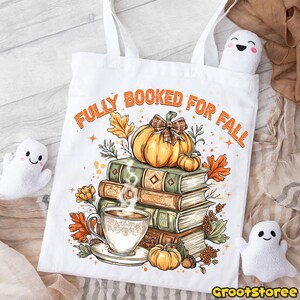 May include: White tote bag printed with "FULLY BOOKED FOR FALL" in orange. The design includes a stack of books, a pumpkin with a plaid bow, a cup of coffee, and autumn leaves. Two small ghost plushies are visible.