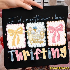 Może przedstawiać: Czarna torba typu tote z napisem "I'd rather be thrifting". Projekt zawiera trzy dekoracyjne ramki ze wstążkami i w&oacute;zek na zakupy wypełniony przedmiotami w stylu vintage. Tekst "Thrifting" jest w kolorowych literach.